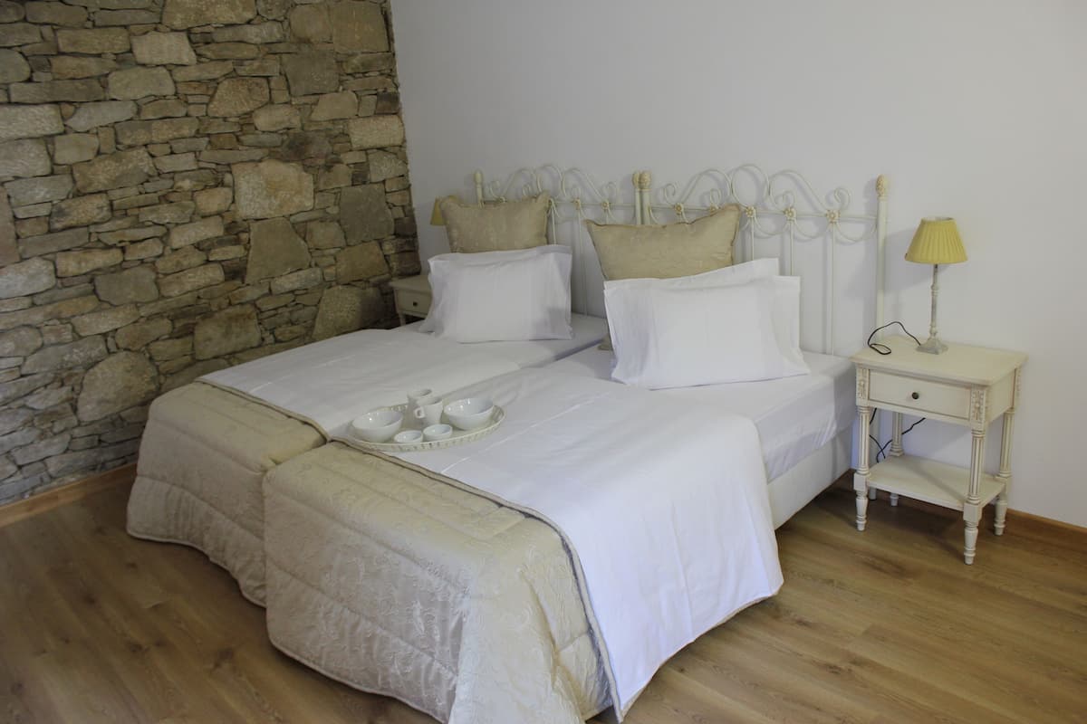 A bedroom with a stone wall, a bed with white bedding, a bedside table with a lamp, and a tray of cups and saucers.