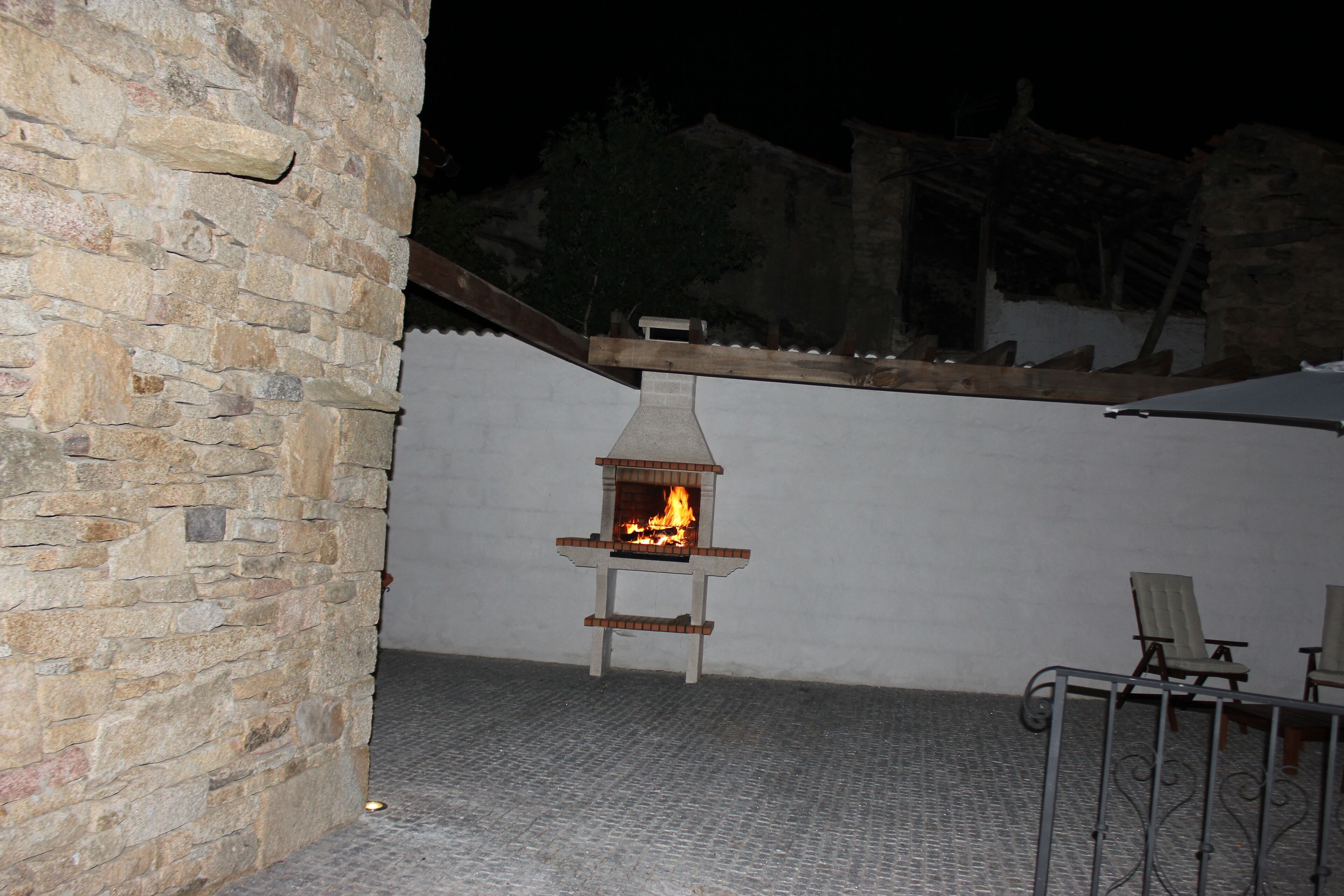 A stone wall with a brick oven, two chairs, and a metal fence in an outdoor setting.
