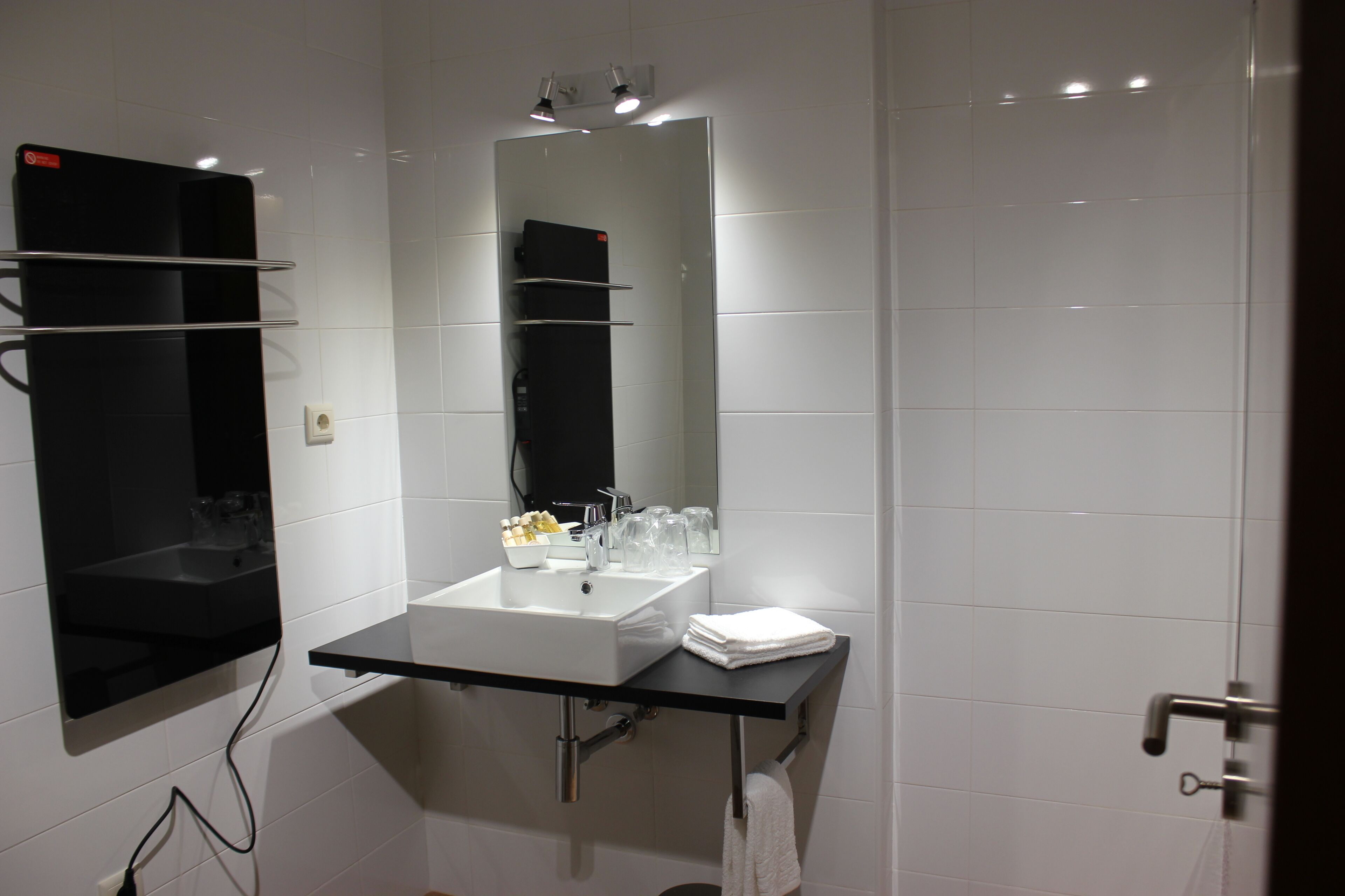 Une salle de bain moderne avec un plan de toilette noir, des carreaux blancs, un grand miroir et un porte-serviettes.