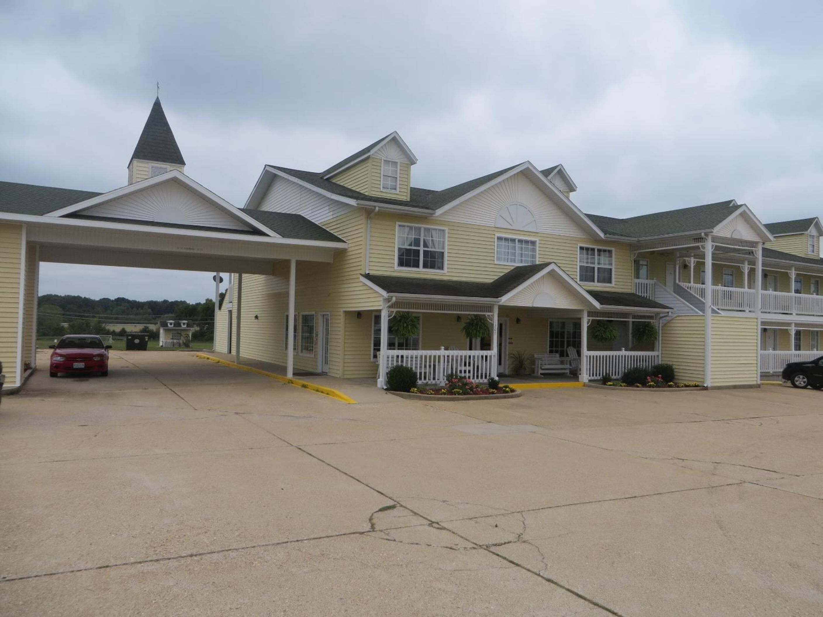 A multi-story motel with a covered parking area and a church steeple in the background.