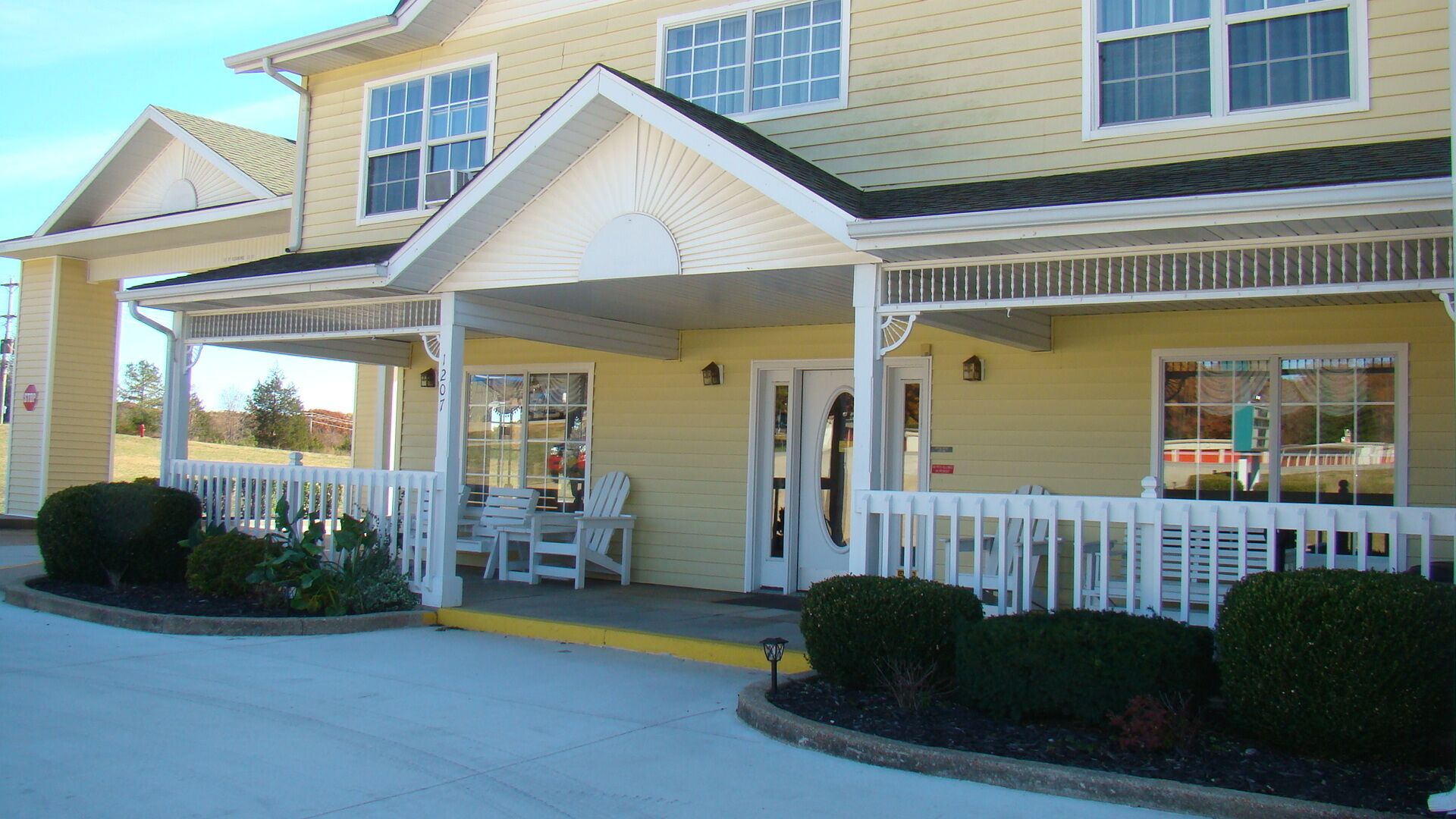 A two-story building with a covered porch, white railings, and a number '207' on the wall.