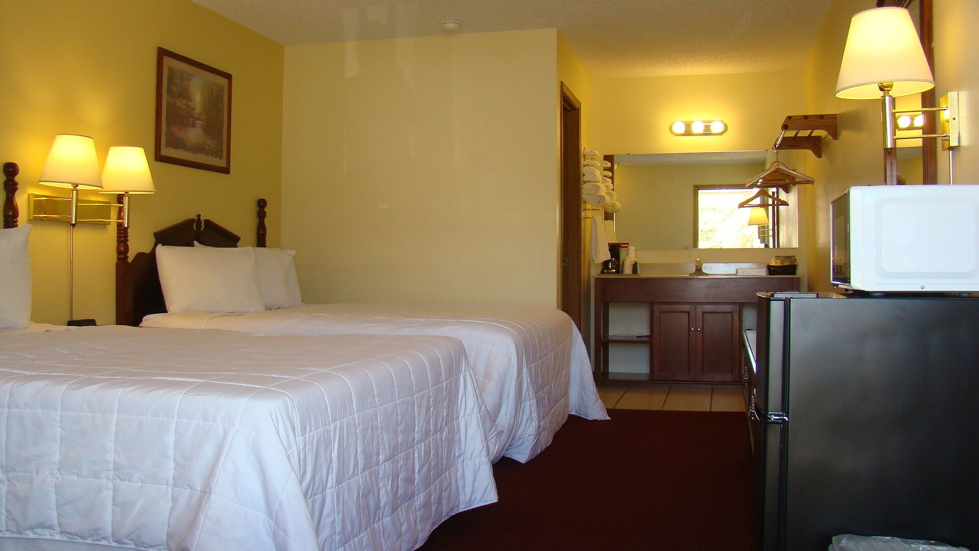 Une chambre d’hôtel avec deux lits, un bureau avec un miroir, un réfrigérateur et un lavabo.
