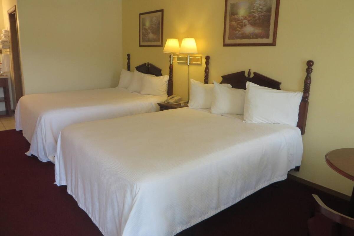 A hotel room with two single beds, a bedside table with a lamp, a phone, and two framed pictures on the wall.