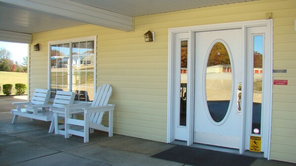 A building with a yellow exterior, a white door with an oval window, and two white Adirondack chairs outside.