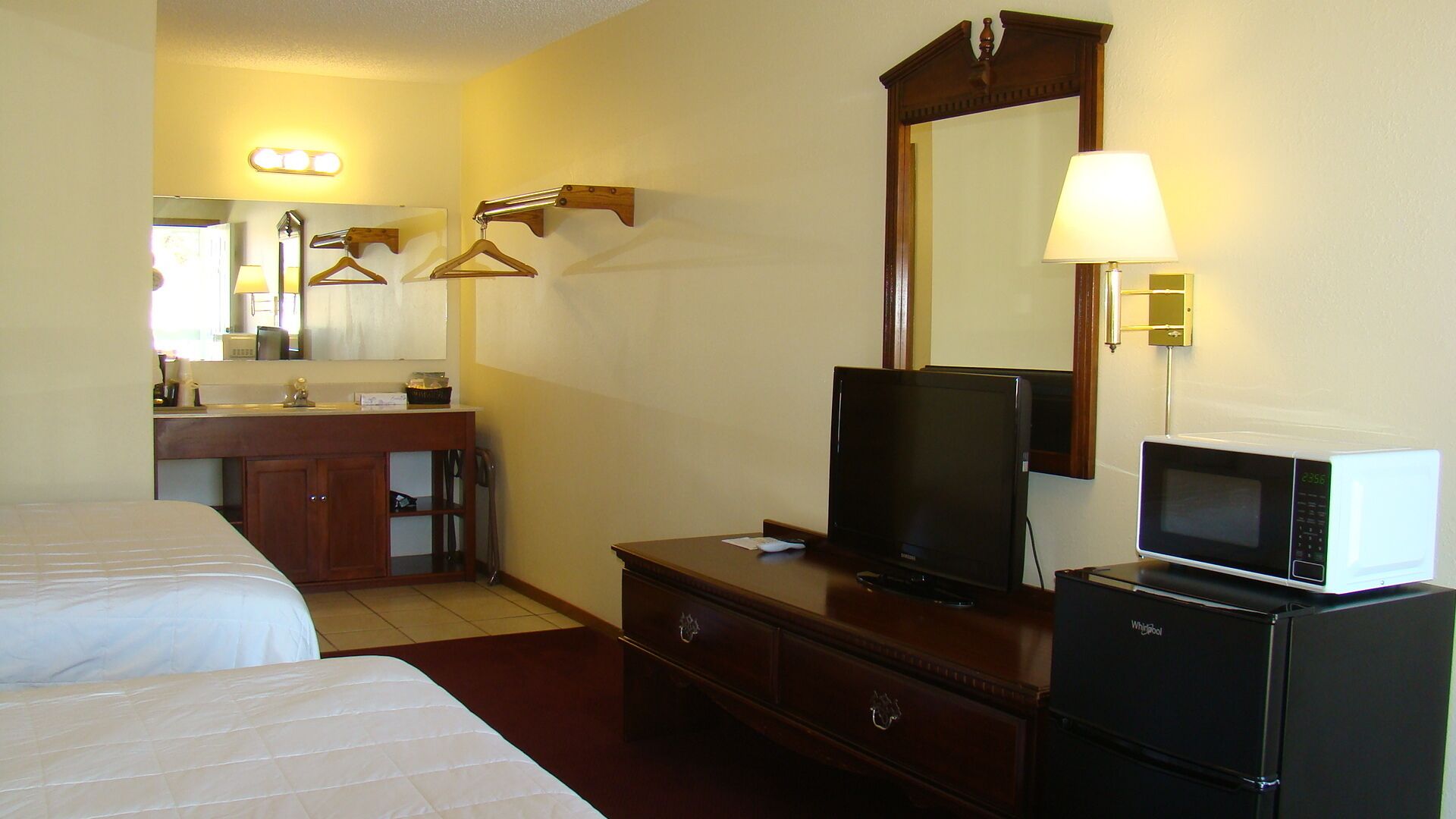 Habitación de hotel con una cama, televisión, microondas, cómoda, espejo y tocador con espejo e iluminación.