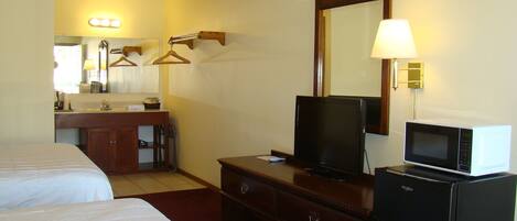 Habitación de hotel con una cama, televisión, microondas, cómoda, espejo y tocador con espejo e iluminación.
