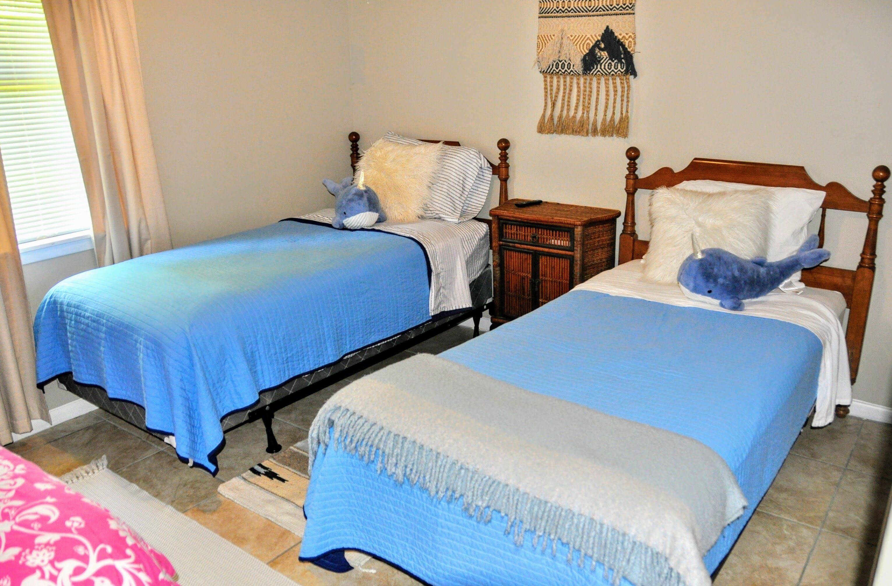 Two twin beds with blue and white bedding, a wooden nightstand, and a wall tapestry.