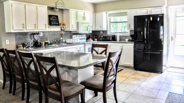 Una cocina moderna con armarios blancos, un refrigerador negro y una isla central con taburetes de bar.