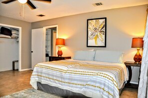 Ein Schlafzimmer mit einem Bett, zwei Nachttischlampen, einem Deckenventilator, einer zur Garderobe führenden Tür und einem gerahmten abstrakten Gemälde an der Wand.