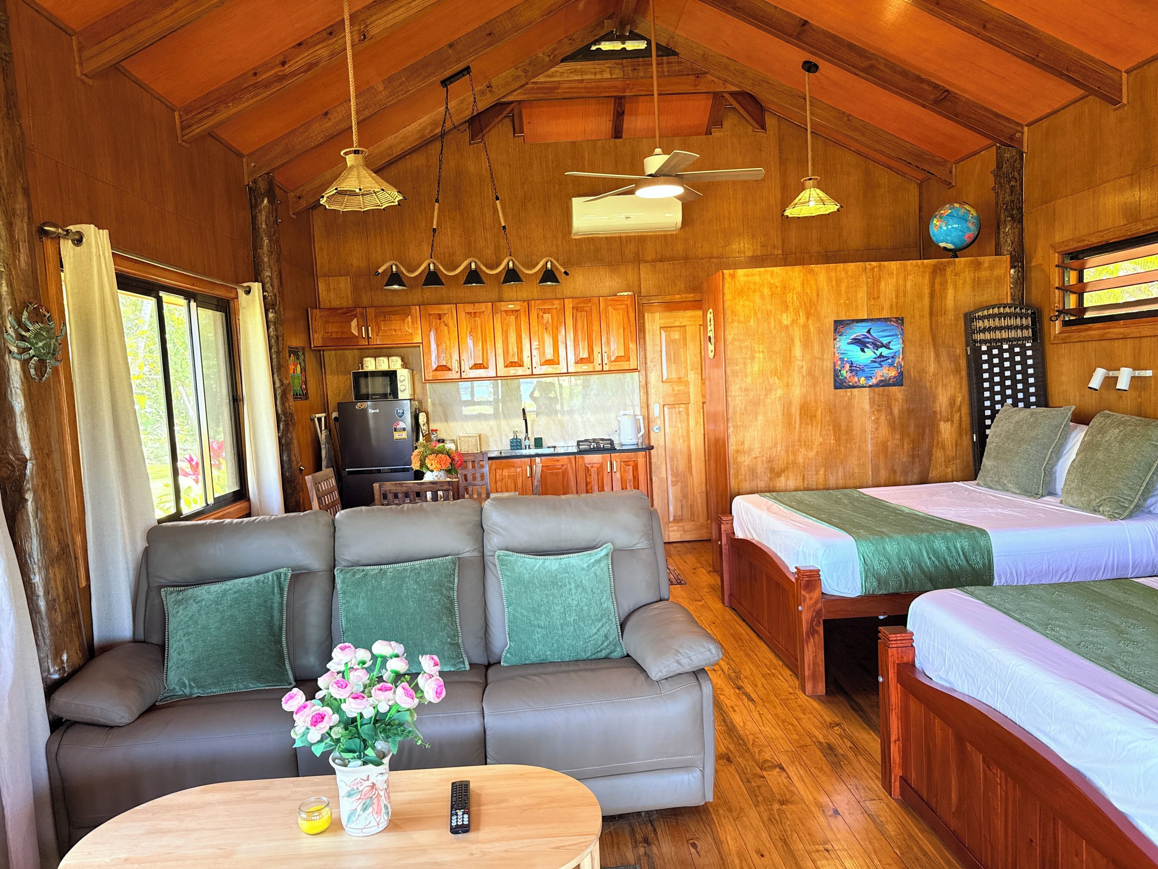 A cozy cabin interior with a sofa, two beds, a dining area, and a kitchen.