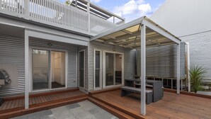 Un patio moderno al aire libre con terraza de madera, zona de estar cubierta y balcón blanco.