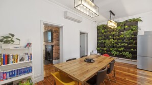 Un comedor con una mesa de madera, sillas, una estantería y un jardín vertical en la pared.