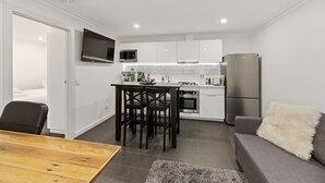 Una cocina moderna con armarios blancos, una mesa de comedor con sillas, un sofá gris y un televisor montado sobre la encimera.