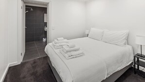 Una habitación de hotel moderna con una cama grande, una mesita de noche con lámpara y un espacio con ducha.