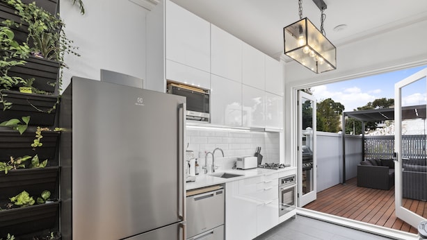 Una cocina moderna con electrodomésticos de acero inoxidable, armarios blancos y vistas a una terraza exterior.