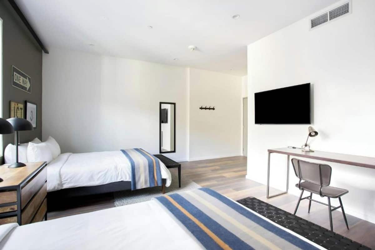 A hotel room with two beds, a desk with a chair, a TV, and a coat rack.
