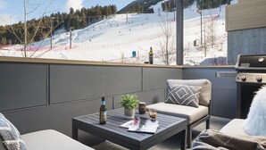 Un balcon avec vue sur une piste de ski, un barbecue et des sièges offrant une vue panoramique.