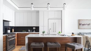 Une cuisine moderne avec des meubles blancs, un îlot central doté de tabourets, un four encastré et un pare-feu noir.