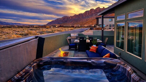 A hot tub with a fire feature, outdoor seating, and a view of a desert landscape with mountains in the background. - Exclusive Retreats White Rim 3369- Luxury Moab Retreat with Private Hot Tub (Moab)