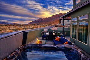 A hot tub with a fire feature, outdoor seating, and a view of a desert landscape with mountains in the background.