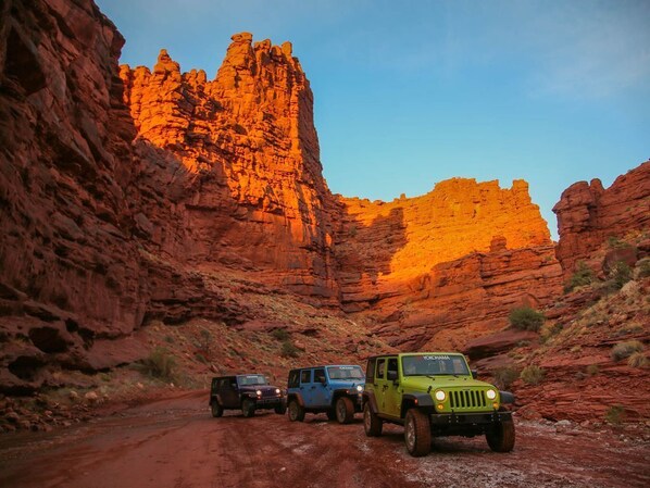 Three off-road vehicles parked on a dirt road in a canyon with red rock formations.