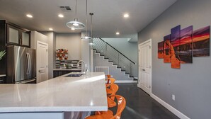 A modern kitchen with a central island, stainless steel appliances, and a staircase leading to another level. - Exclusive Retreats White Rim 3369- Luxury Moab Retreat with Private Hot Tub (Moab)