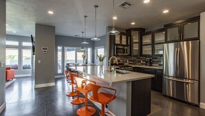 A modern kitchen with a central island, stainless steel appliances, and orange bar stools. - Exclusive Retreats White Rim 3369- Luxury Moab Retreat with Private Hot Tub (Moab)