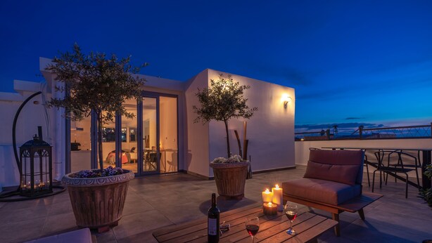 A terrace with a sofa, a table with wine, candles, and potted plants. - Mythos Luxury Suites (Athens)