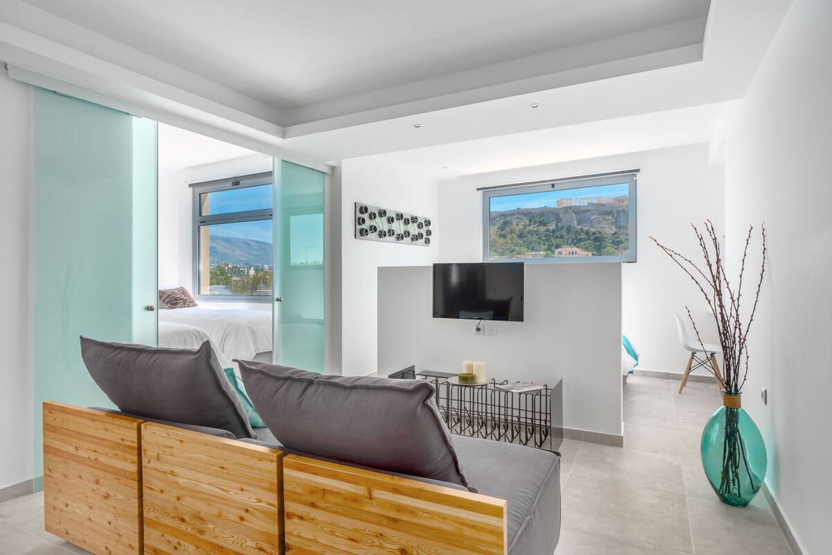 Una habitación de hotel moderna con cama, zona de estar, televisor y vista a la ciudad.