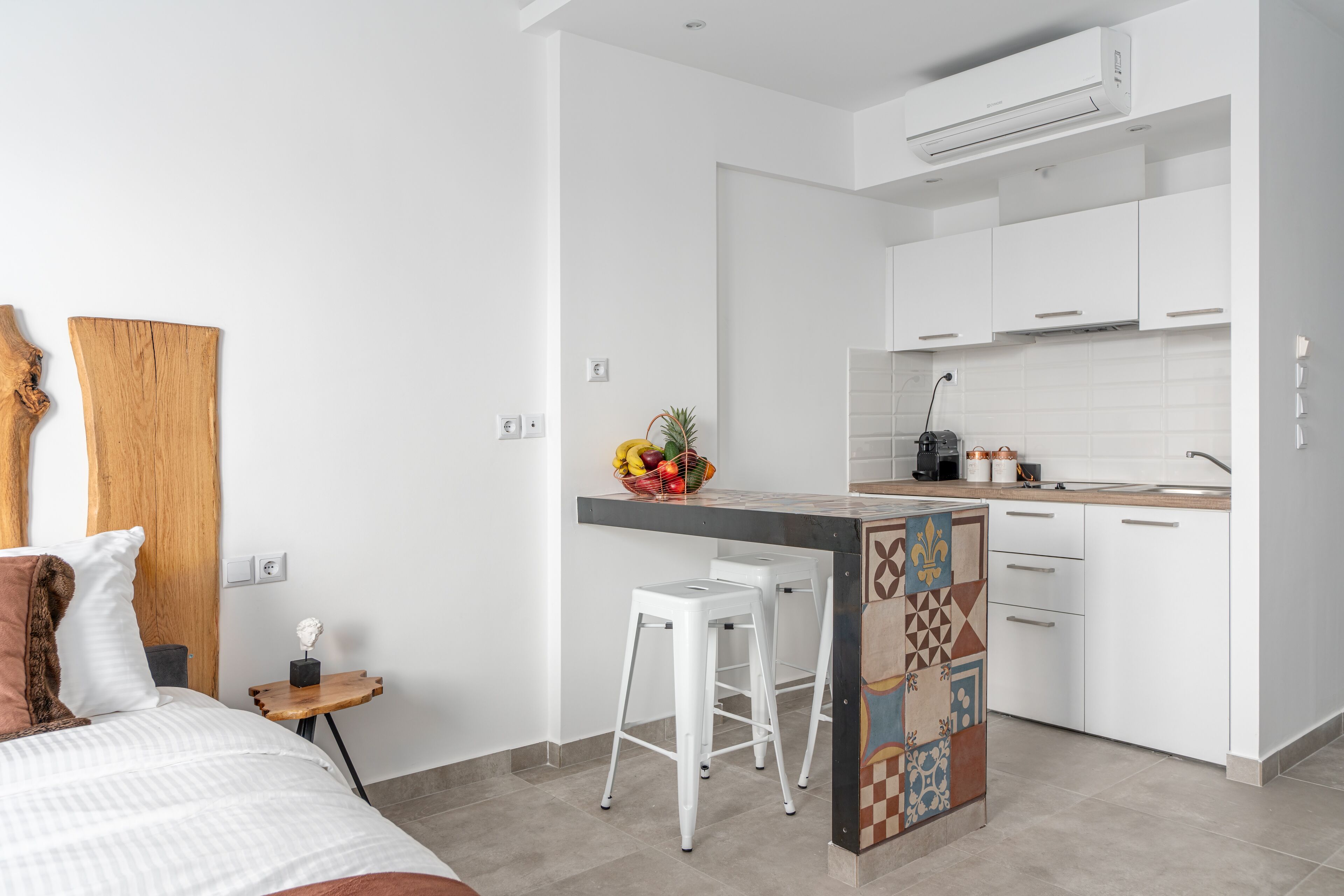 Una cocina moderna con armarios blancos, una isla central con taburetes y un frutero en la encimera.