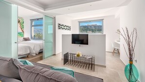 A modern, open-plan living space with a bed, a dining area, and a TV mounted on the wall. - Mythos Luxury Suites (Athens)
