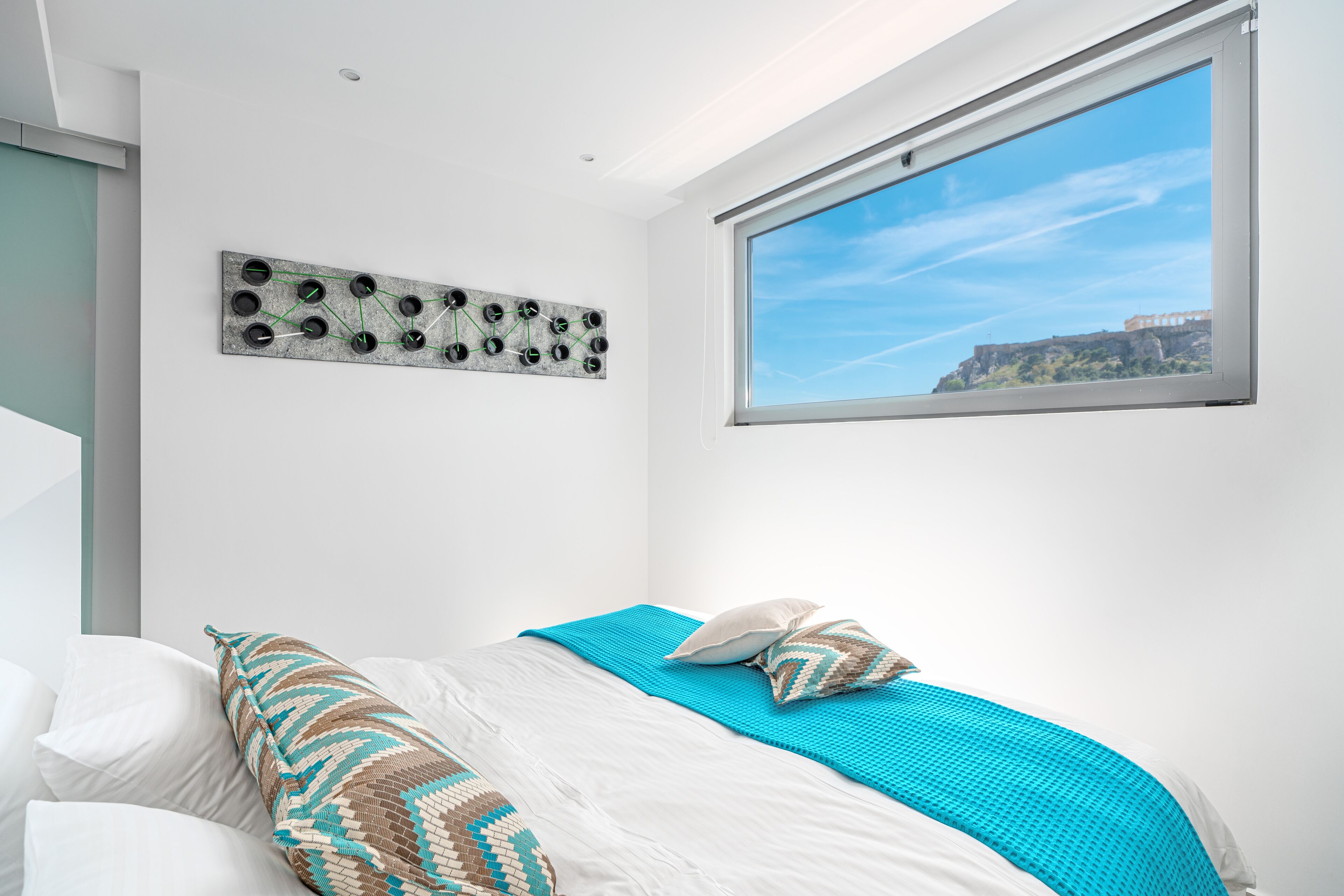Un dormitorio con cama, ventana con vista a un edificio y una obra de arte colgada en la pared.