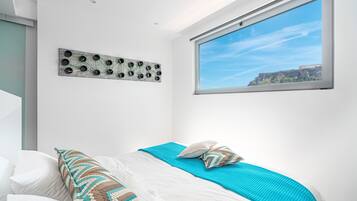 Un dormitorio con cama, ventana con vista a un edificio y una obra de arte colgada en la pared.