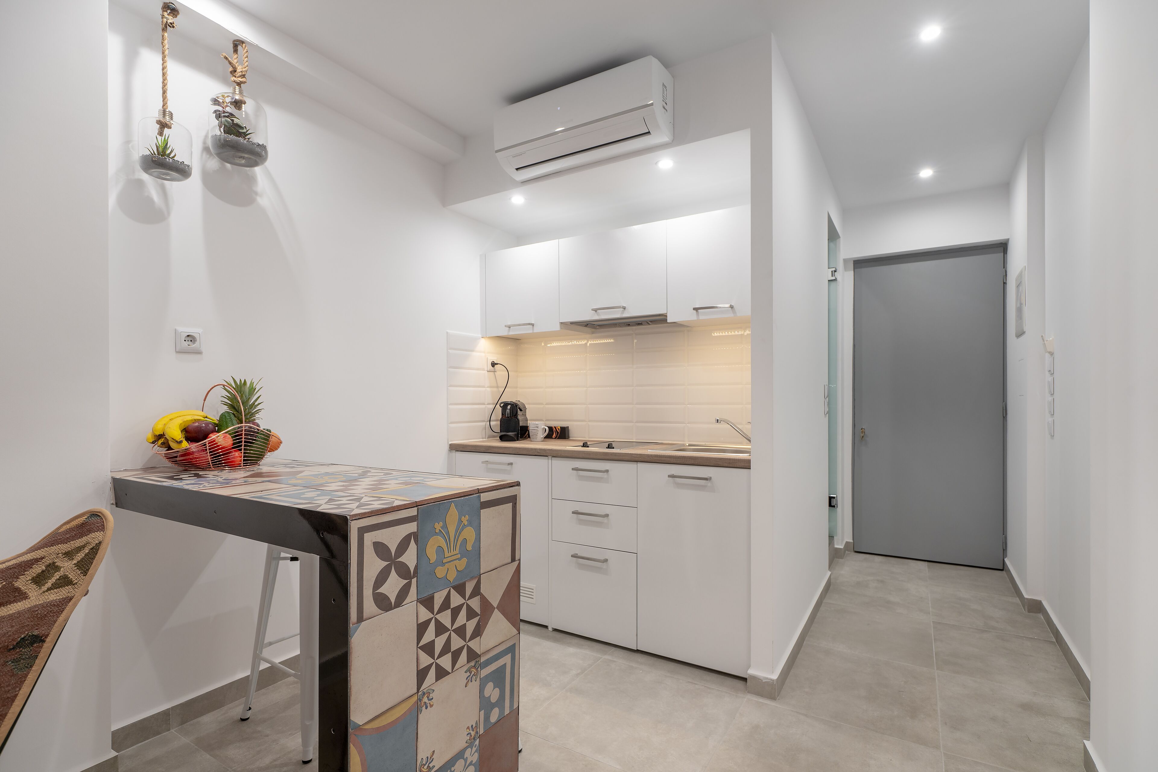 Una cocina moderna con armarios blancos, salpicadero de azulejos y una cesta de fruta en la encimera.