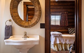 A bathroom with a wooden-framed mirror, a white sink, and a towel hanging on a metal ring. - Scout's Rest in Cody - Beautiful Cozy Log Cabin that sleeps 8! (Cody)