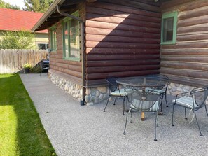 A log cabin with a stone foundation, a patio with a round table and chairs, and a wooden fence in the background. - Scout's Rest in Cody - Beautiful Cozy Log Cabin that sleeps 8! (Cody)