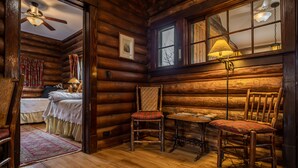 L’intérieur d’un chalet confortable en rondins de bois, avec un lit, une chaise en bois, une table et une fenêtre avec une lampe.