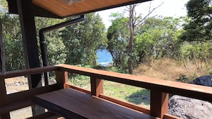 A wooden deck with a bench, overlooking a natural landscape with trees and a body of water. - Yakushima South Coast House (Yakushima)