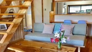 A modern living room with a wooden staircase, a sofa with patterned cushions, and a wooden coffee table with a vase of flowers. - Yakushima South Coast House (Yakushima)
