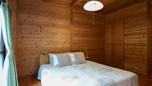 A wooden-paneled bedroom with a bed, curtains, and a hanging light fixture. - Yakushima South Coast House (Yakushima)