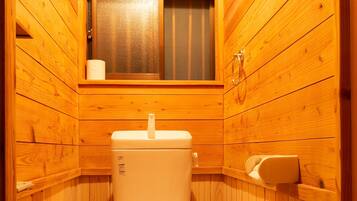 A small, wooden-paneled bathroom with a toilet, a window, and a shelf with a tissue box.