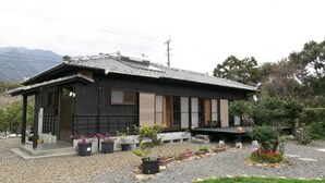 Une maison traditionnelle japonaise, avec un toit en tuiles, une façade en bois et une allée gravillonnée.