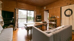 L’intérieur chaleureux d’un chalet avec un plafond en bois, une table à manger, un canapé et une grande fenêtre agrémentée de rideaux.