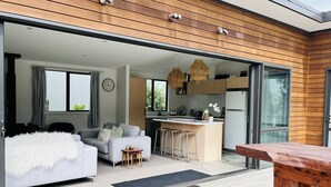 Un espacio habitable moderno y abierto con sofá, mesa de comedor y zona de cocina con refrigerador y taburetes de bar.