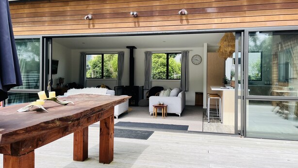 Un interior moderno con una mesa de comedor de madera, un sofá blanco y un puerta de cristal que da a un balcón.