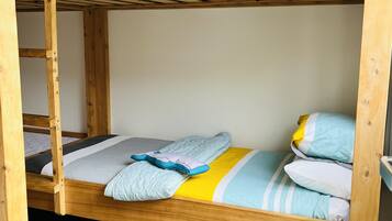 A bunk bed with a wooden frame, a grey mat at the foot of the bed, and a grey wall in the background.