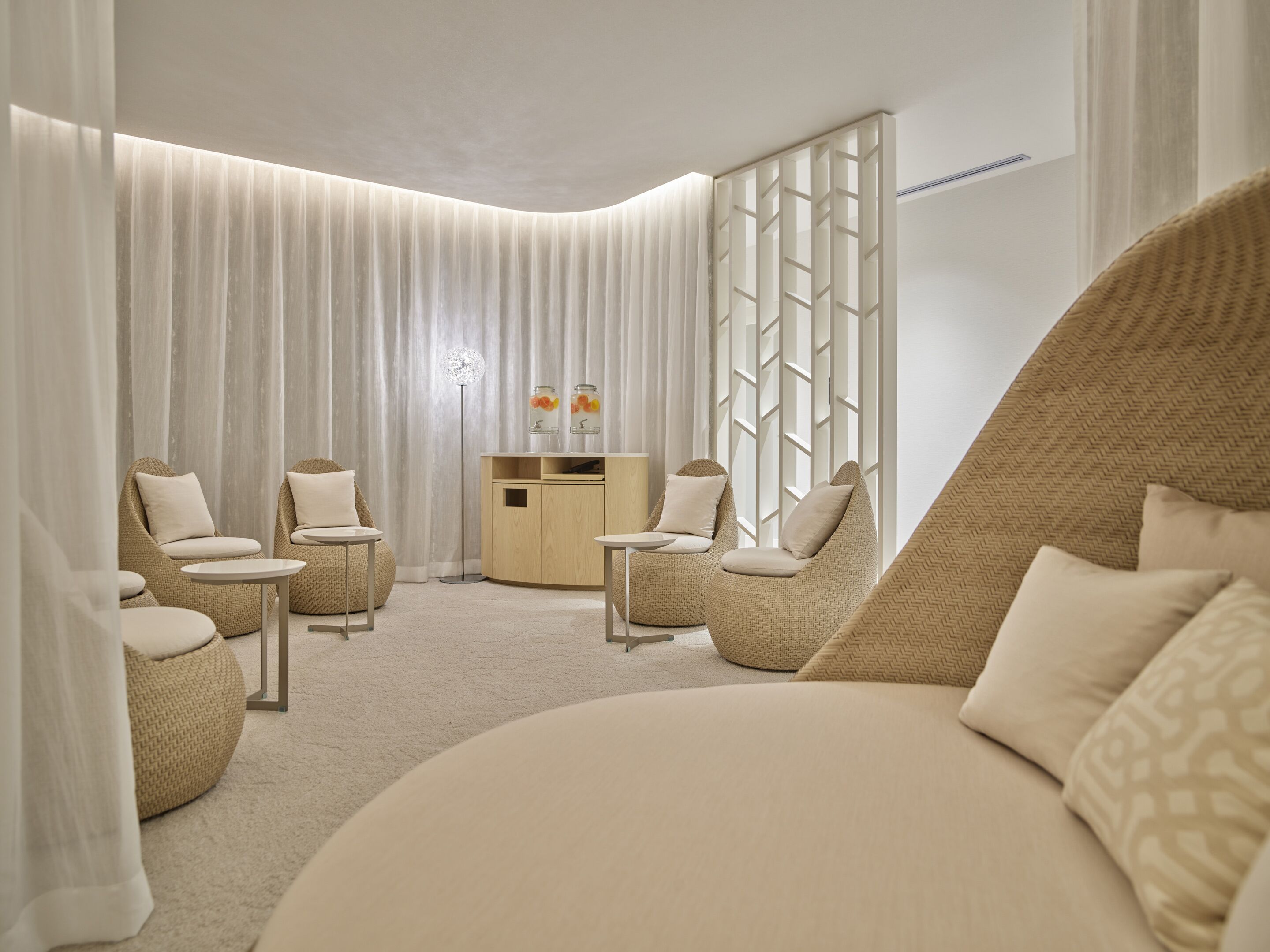 Een moderne hotelkamer met een gebogen bed, twee fauteuils, een bijzettafeltje, een houten kast en een vloerlamp.