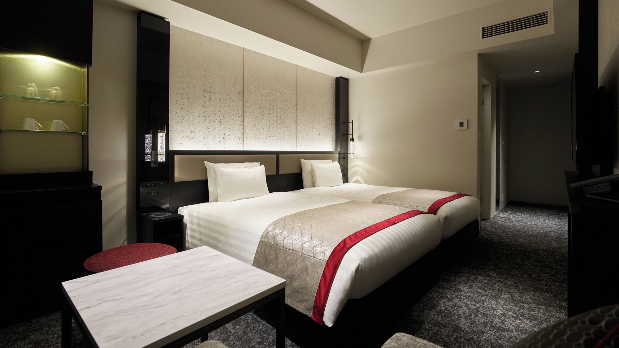 A hotel room with a large bed, a bedside table, a TV, and a minibar.