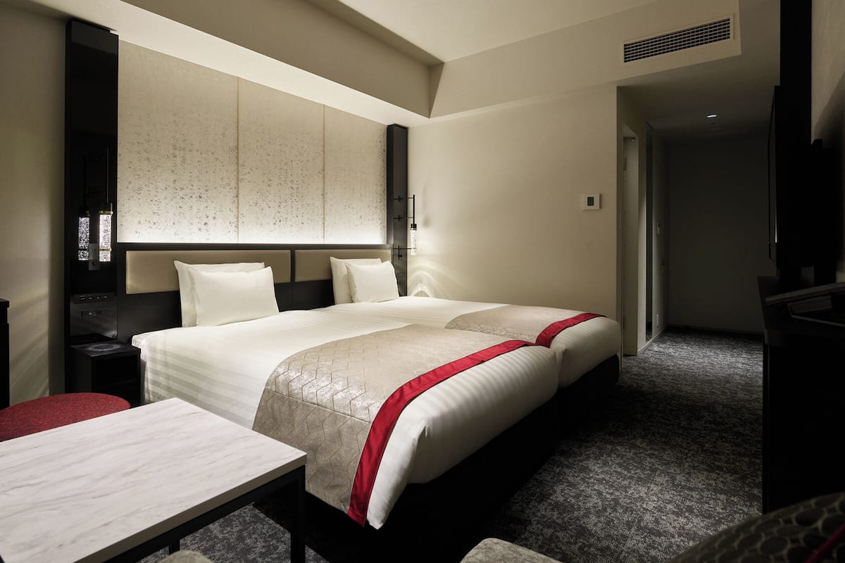 A hotel room with a large bed, a bedside table, a TV, and a minibar.