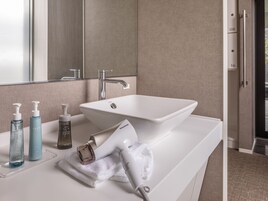 Un baño con lavamanos blanco, espejo y artículos de aseo en la encimera.